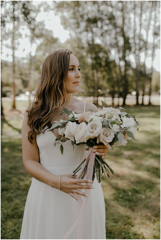 A wedding bouquet featuring elegant blush and ivory roses, complemented by delicate greenery. The bouquet is arranged in a classic, sophisticated style, perfect for a refined and timeless wedding celebration.